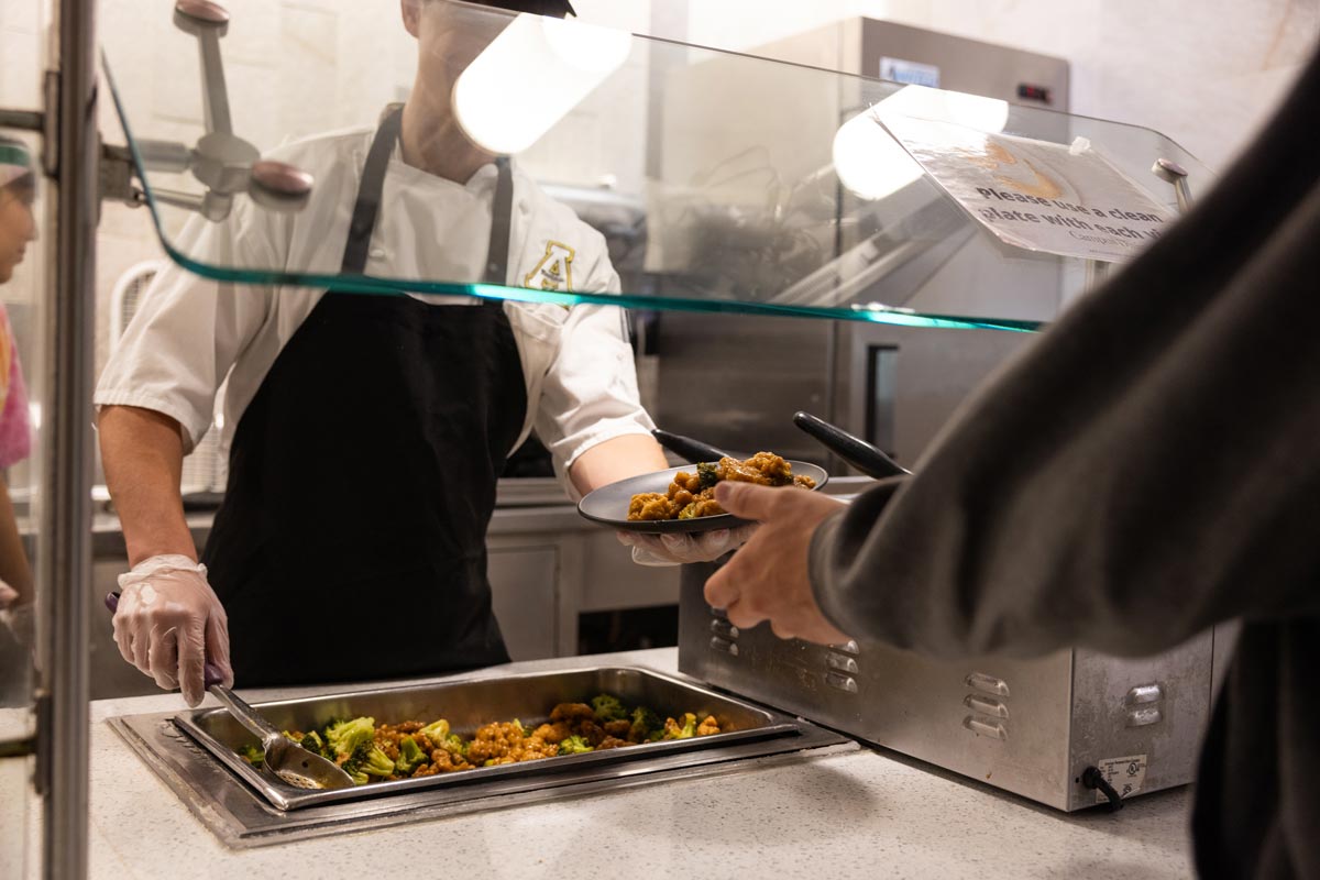 Server handing a plate of chicken and broccoli to customer