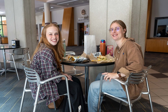 Two female students smiling and enjoying a meal together