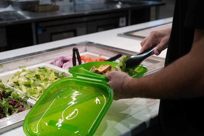 Student filling takeout container with food.